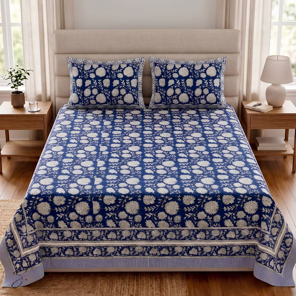 A neatly made bed in a bright bedroom setting, covered with a blue and white floral patterned bedsheet and matching pillowcases.