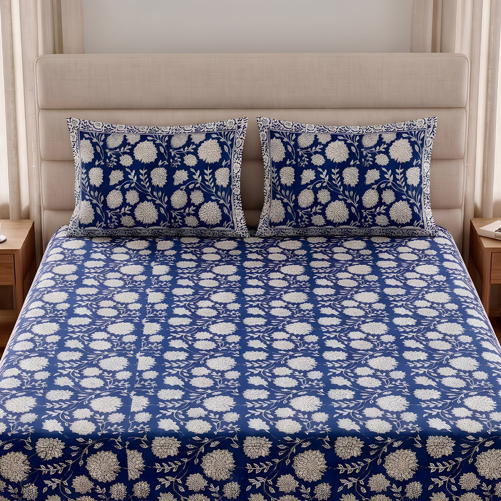 A neatly made bed with a blue and white floral print bedsheet and two matching pillowcases, set against a beige upholstered headboard in a bedroom.