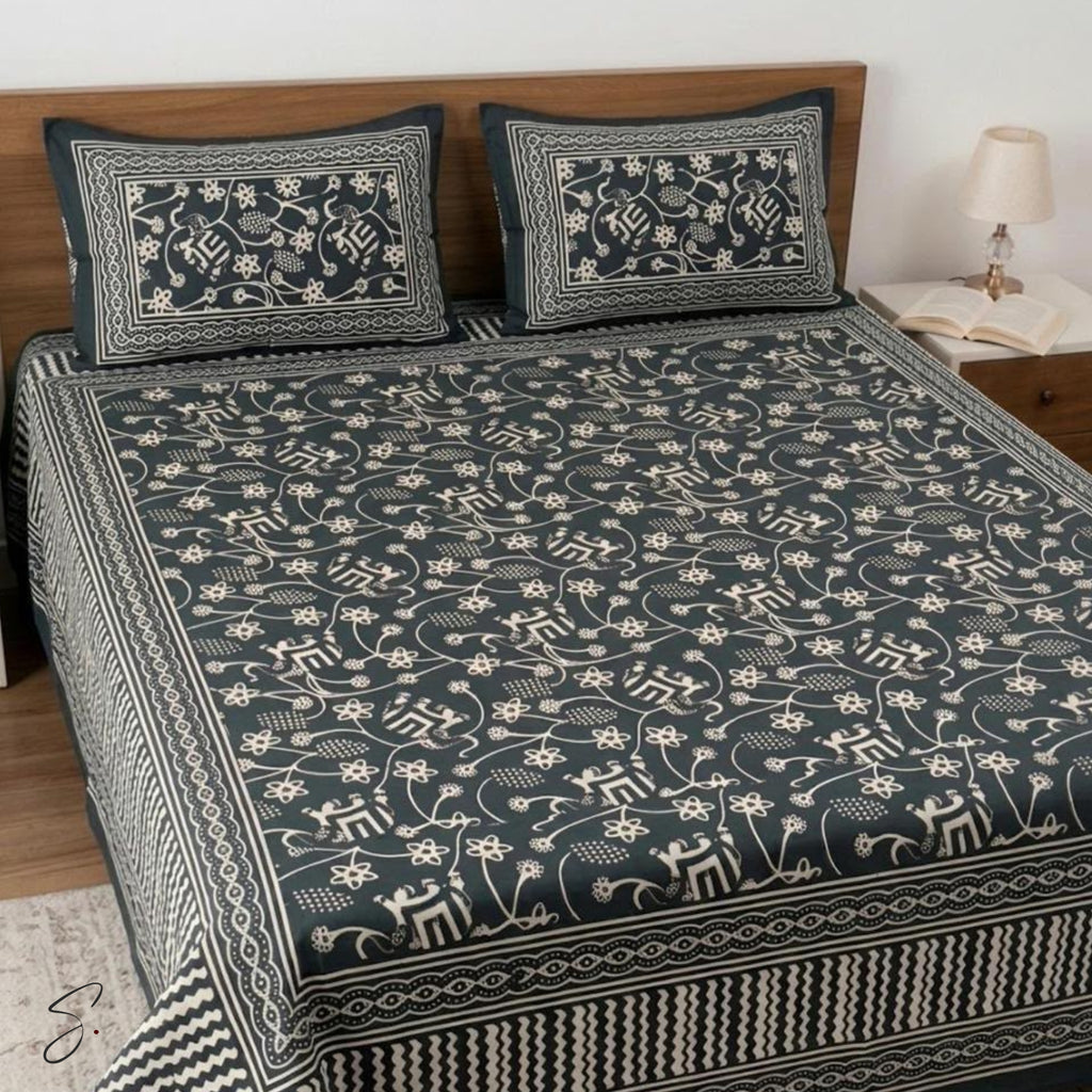 A dark charcoal gray block-print cotton bedding set featuring an intricate cream floral and deer pattern, styled on a bed with matching pillowcases in a bedroom setting.